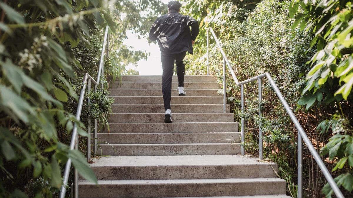 A man in sports clothing running up steps outdoors surrounded by greenery.